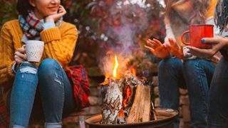 Three females best friends sitting around bonfire in casual clothes warming