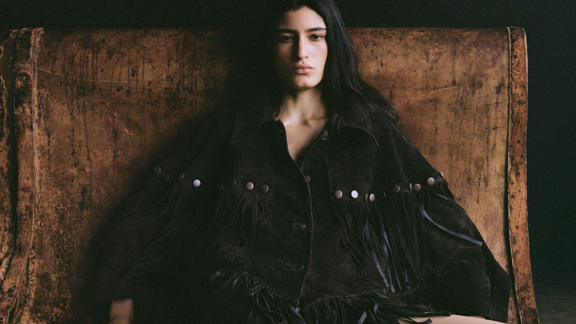 a model wearing a fringe suede jacket in front of a wood backdrop