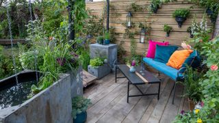 water tank with rain chains on small decked area with garden sofa and table, and lots of planting