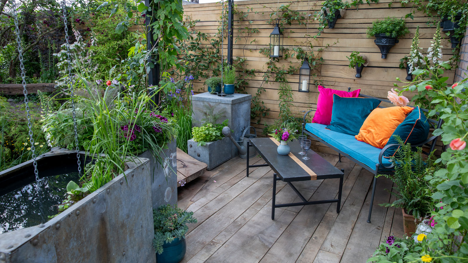 water tank with rain chains on small decked area with garden sofa and table, and lots of planting