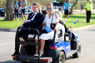 Robert MacIntyre and girlfriend Shannon Hartley arrive at the 2023 Ryder Cup opening ceremony on the back of a golf cart while holding small Team Europe flags