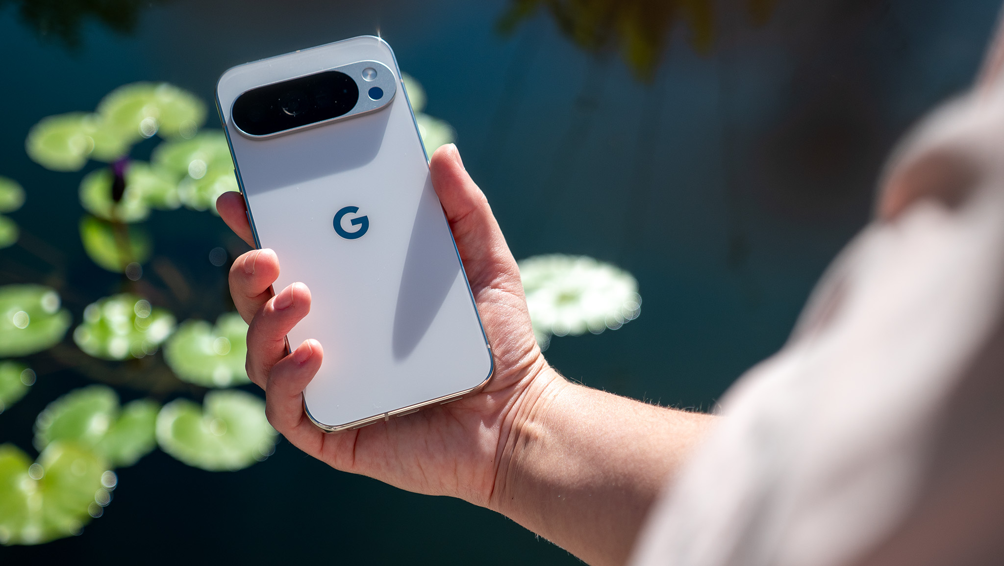Holding a white Google Pixel 10 Pro XL in front of a pond filled with lily pads