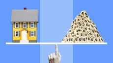 Model of yellow house and a pile of money bags balancing on scales held up by woman's finger, striped blue background