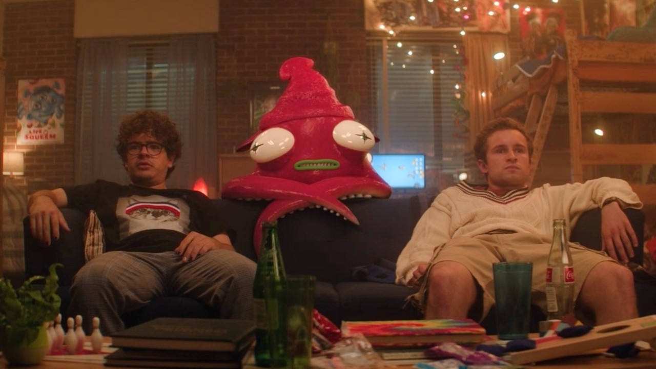 Gaten Matarazzo and Sean Giambrone stting on a couch with an animated pink squid leaning on the couch behind them.