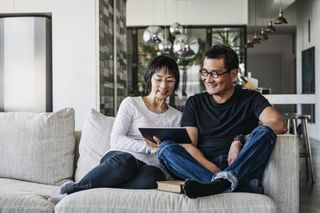Senior woman and mature man using digital tablet at home in living room talking online facetime social media