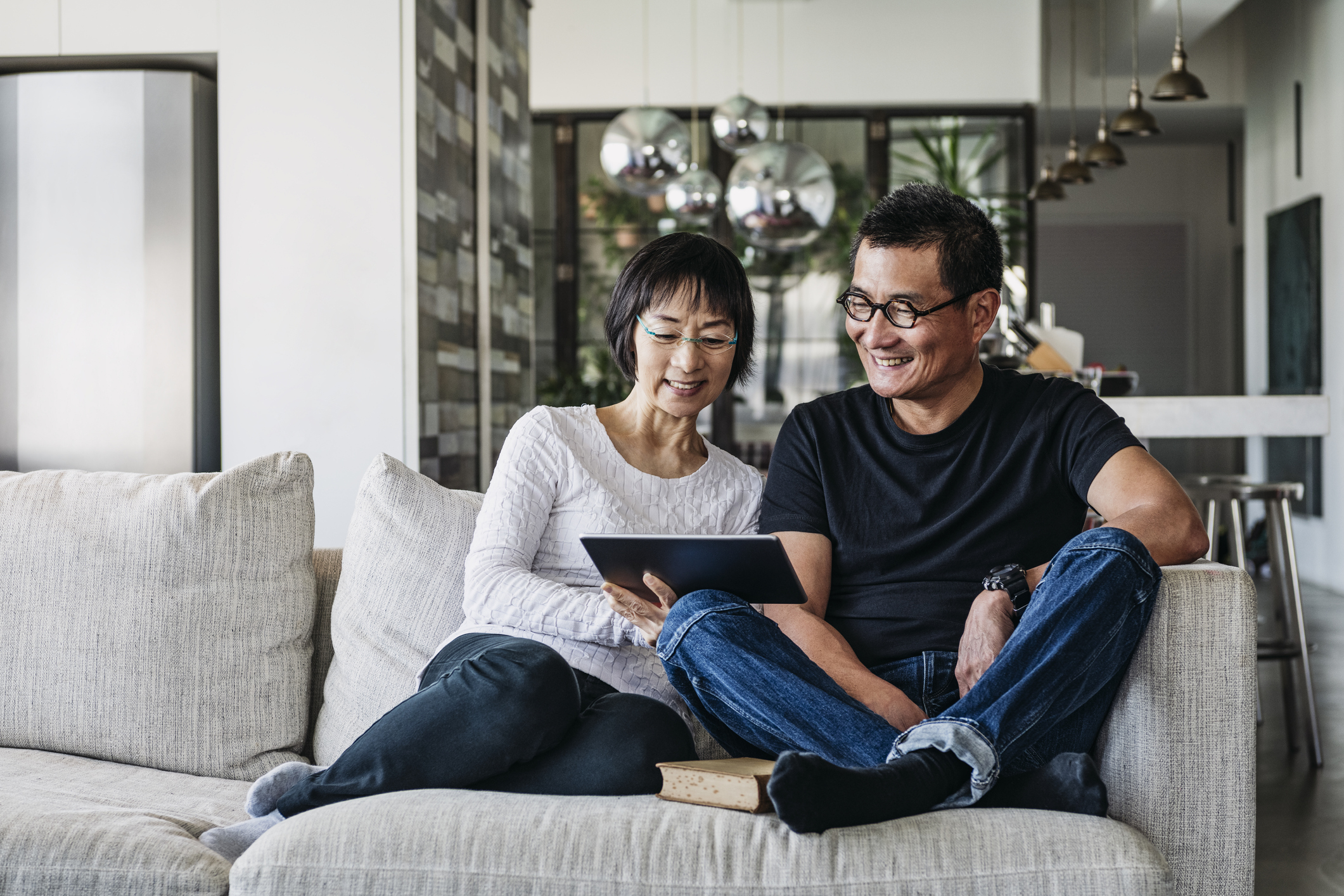 Ältere Frau und reifer Mann, die zu Hause im Wohnzimmer ein digitales Tablet verwenden, um online über soziale Medien zu sprechen