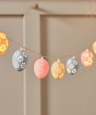 A cream door with six mustard yellow, light blue, and peach pink egg lights with floral cut-out patterns on them