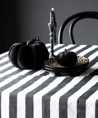 black and white striped beetlejuice halloween table with black pumpkins and a candlestick