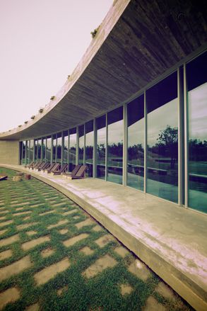 Front view of the eco-resort Rio de Prado, with floor-to-ceiling windows, a sitting area, and a lawn.