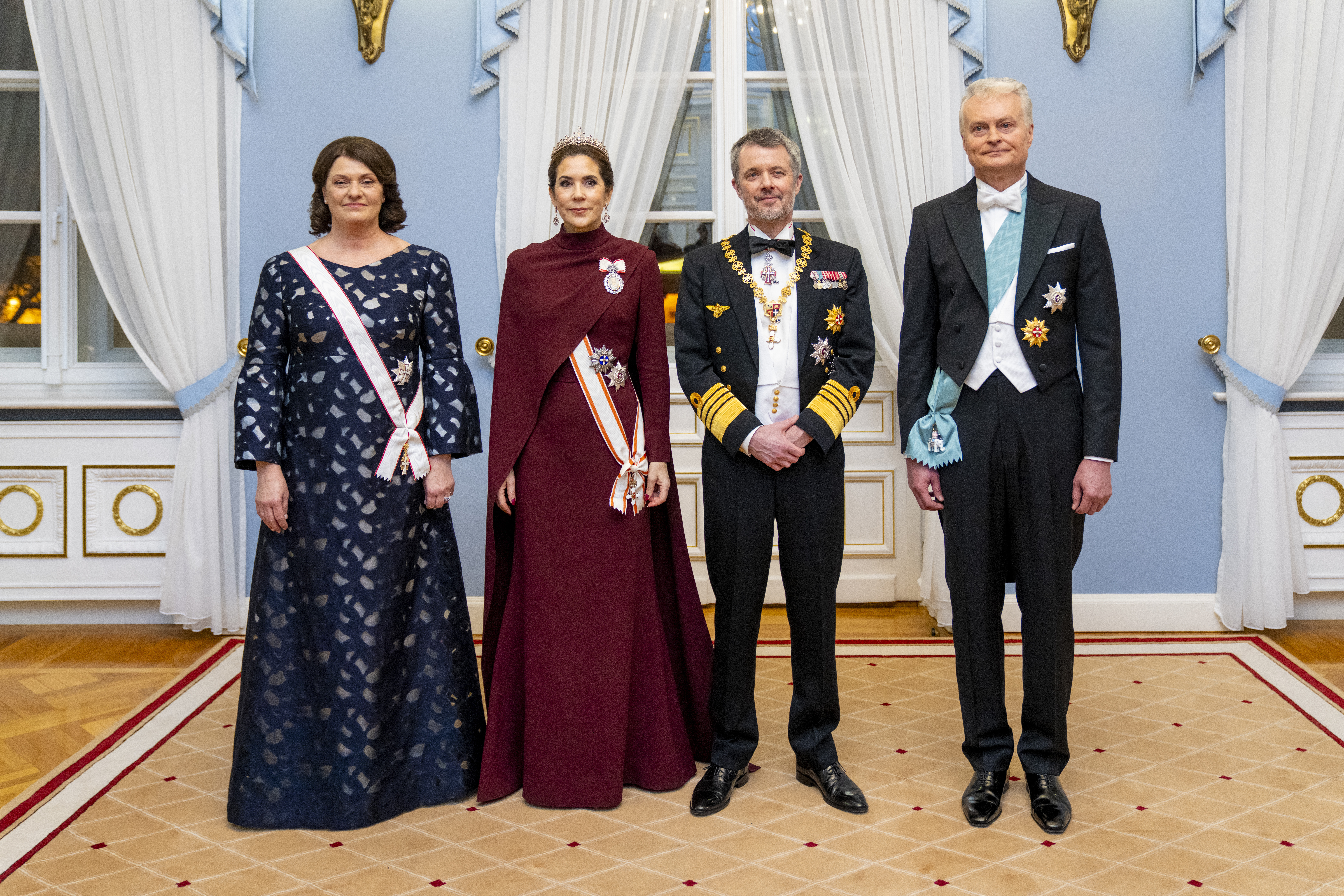 Queen Mary wearing a maroon gown posing with King Frederik and leaders of Lithuania at a banquet