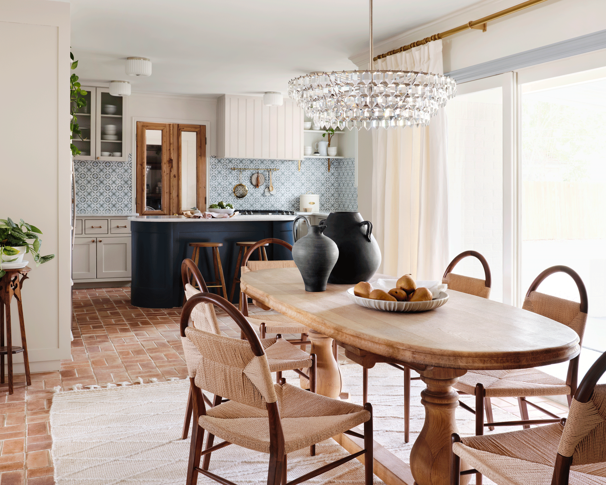 wooden dining room table with rattan chairs, and a kitchen in the background with a large blue island, and tile flooring