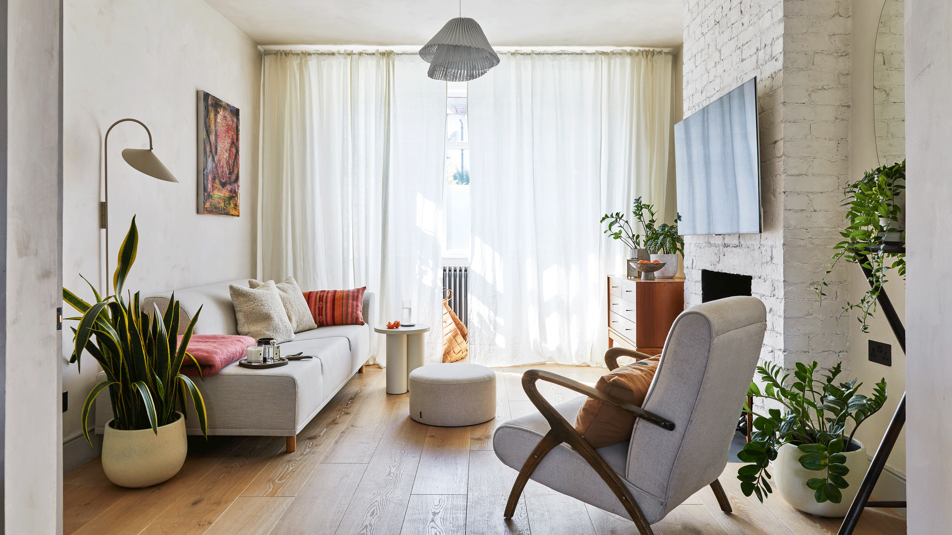 an open plan living room with a large window, a modern sofa, vintage armchair, exposed brick chimney breast