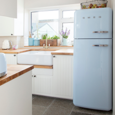 White fitted kitchen, panelled units, wood worktop, blue fridge freezer, twin sink.