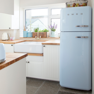 White fitted kitchen, panelled units, wood worktop, blue fridge freezer, twin sink.