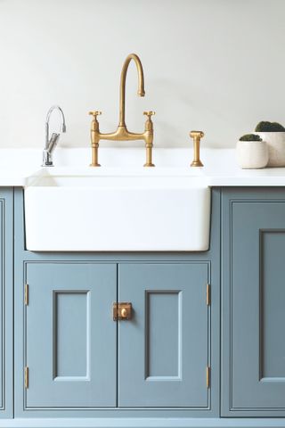 A kitchen ceramic kitchen sink with a tall brass faucet