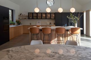 An L shaped kitchen with wooden cabinets and tan leather bar stools with a row of opal glass pendant lights