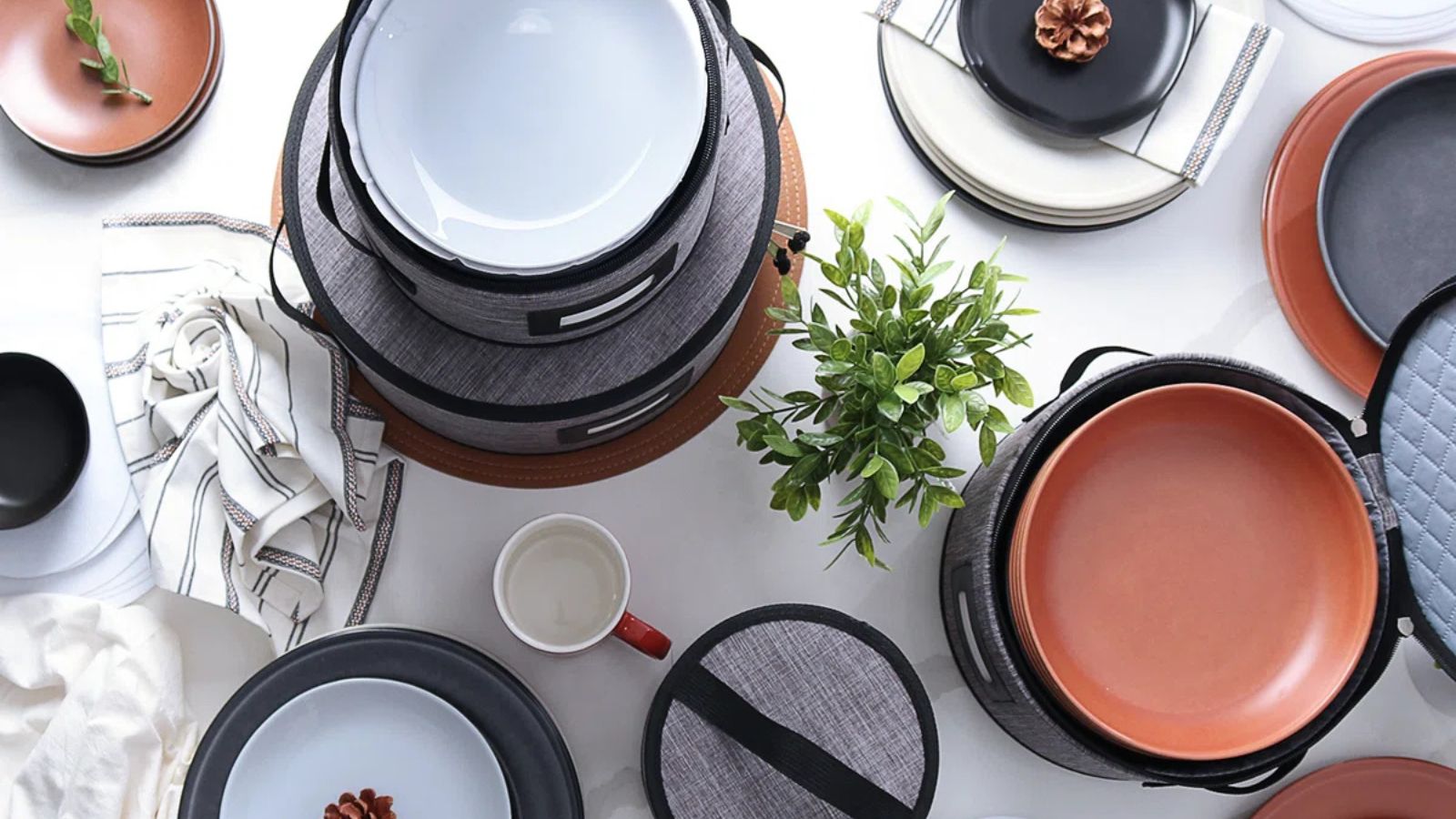 A set of grey hard shell dinnerware storage with crockery on a white table, viewed from above. 