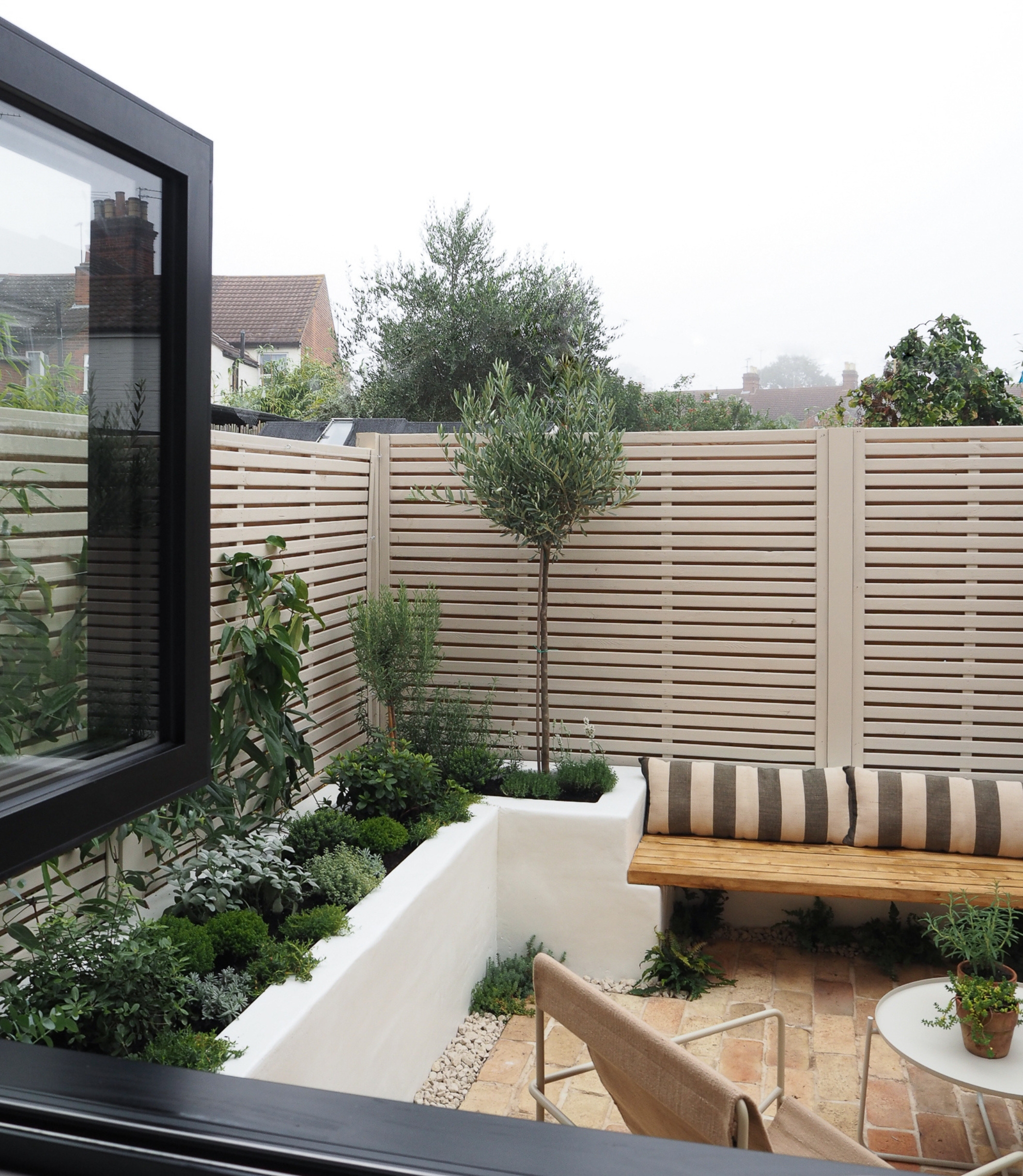 a small mediterranean garden with a brick floor and slatted modern fence