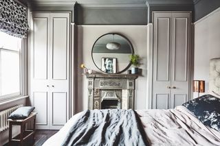 Bedroom in Victorian house with a fireplace, large circular mirror and full length wardrobe doors