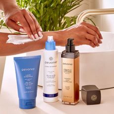 Woman washing her arm in bathroom, three Pevonia products lined up next to her.