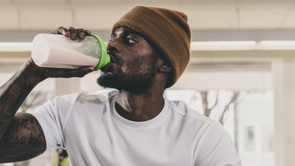 Vegan vs whey protein powder: pictured here, an attractive young man in a beanie hat drinking a protein shake 