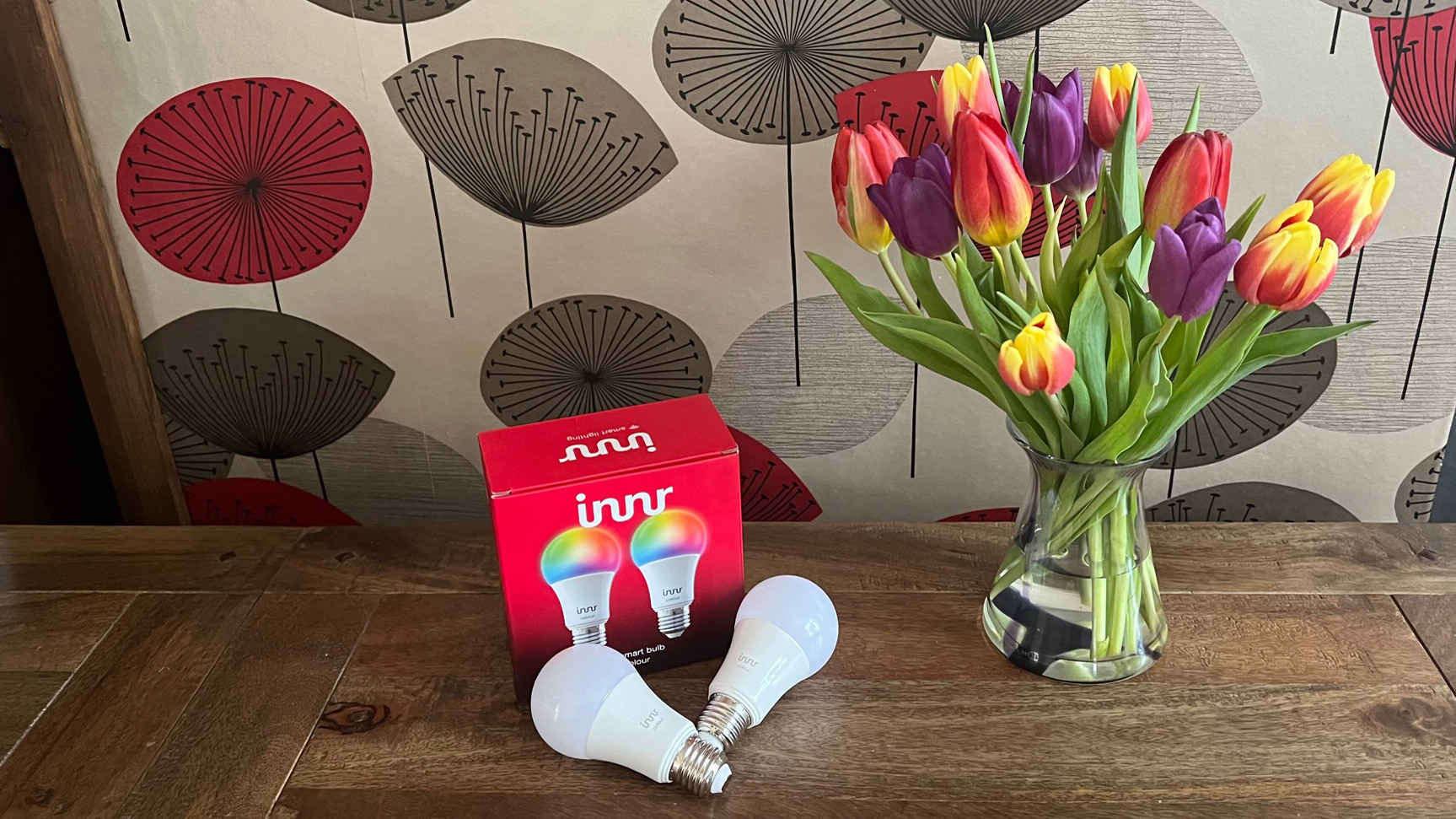 Innr Smart Bulb Color di sebelah kotaknya dan buket bunga tulip dalam vas