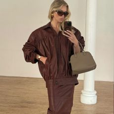 Elsa Hosk takes a mirror selfie wearing a brown leather jacket with a brown leather pencil skirt.