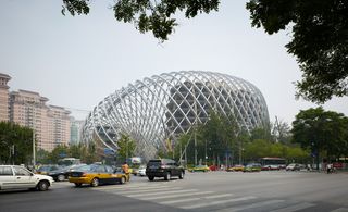 Exterior view of the curved, irregular shaped Phoenix TV building framework during the day. Two buildings are housed within the framework and there are trees, buildings and a road with multiple vehicles nearby