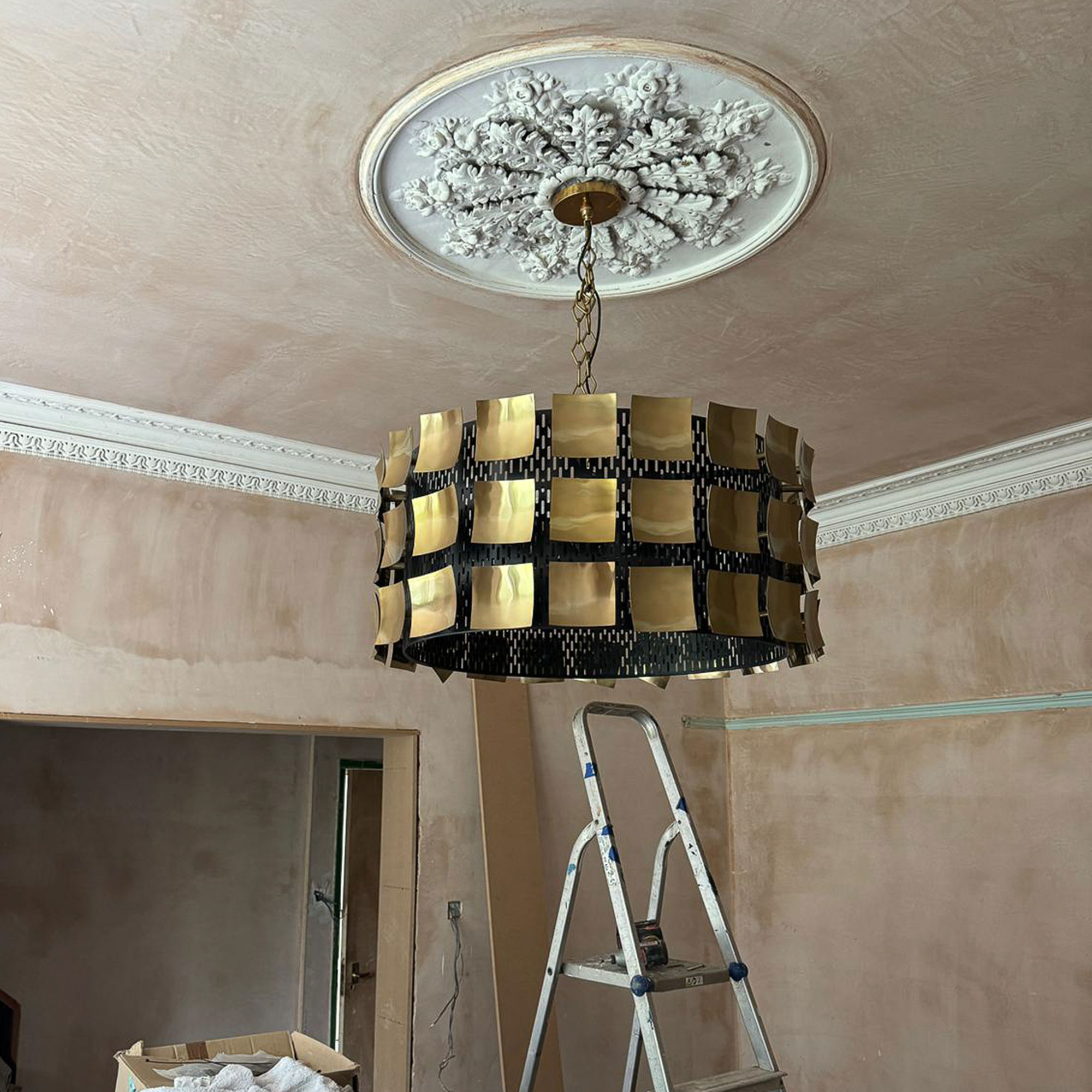Brass chandelier installed in ceiling rose in unfinished room, with stepladder nearby