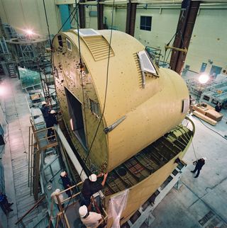 The crew module is being lowered into the lower forward fuselage at the Rockwell Palmdale facility on January 20, 1988.