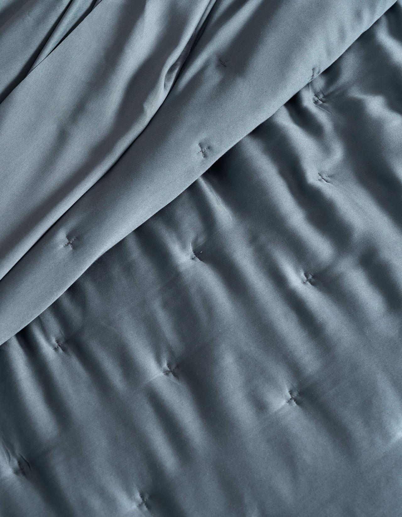 a close-up look of a blue quilt with tufting details (marketing image).