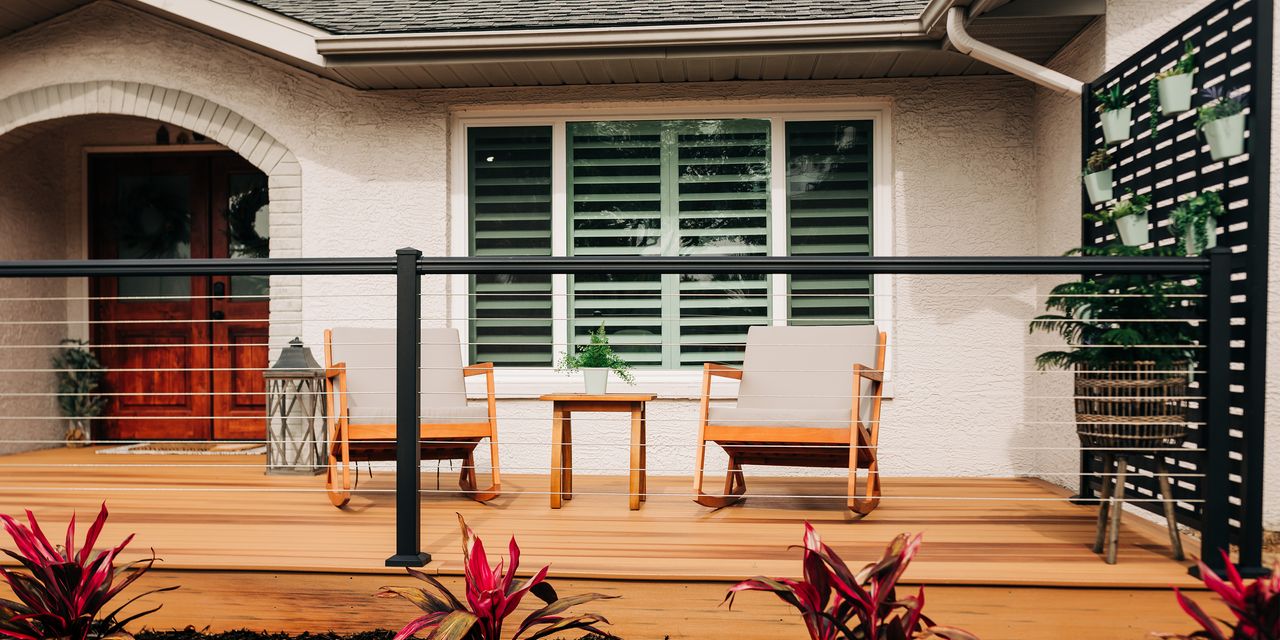 deck area in the front of a house with two chairs and a small table, plus a vertical planter