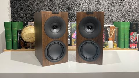 KEF Q Concerto Meta standmount speakers on white table in front of busy bookshelf