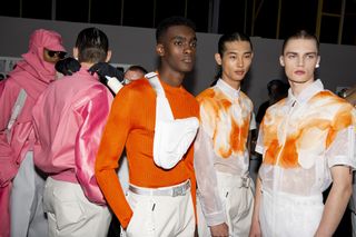 Three models in orange and white outfits. Two other models in the background in pink and white