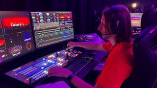 A high school student works a mixing board in an upgraded auditorium. 