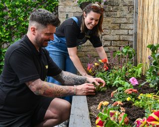man and woman planting flowers in a flower bed