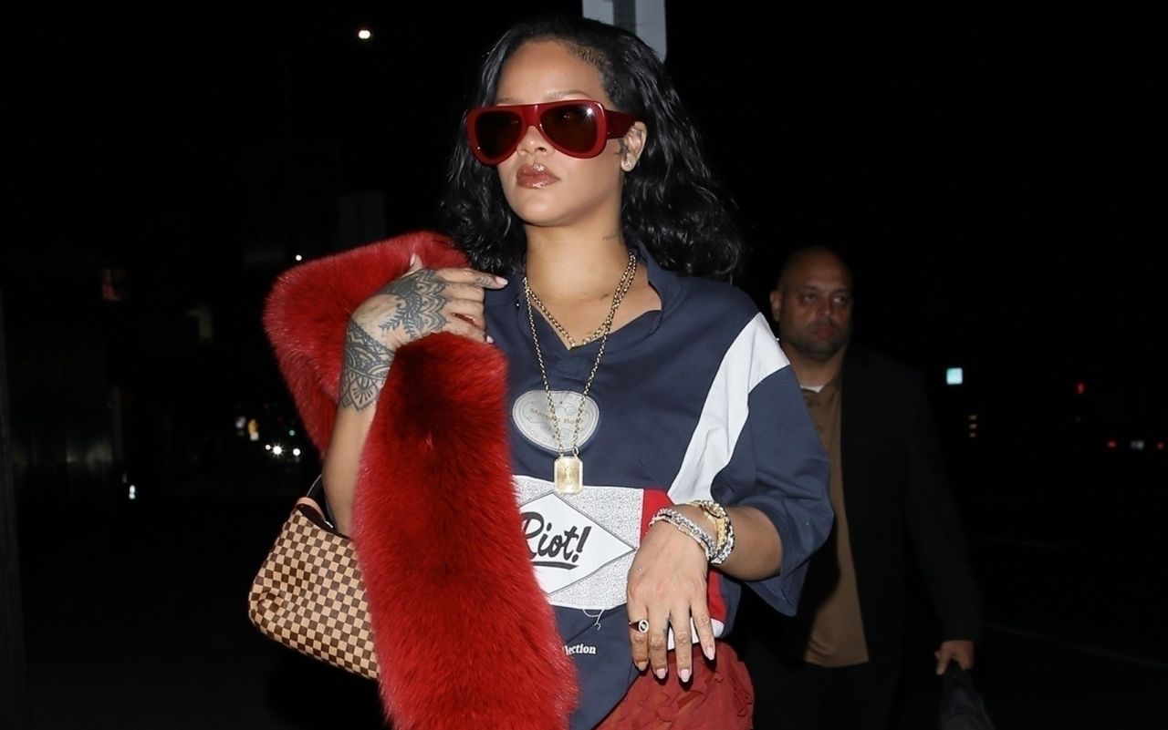 Rihanna walking into a club wearing a red fox stole and carrying a Louis Vuitton bag