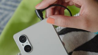 A hand pushing a headphone jack into a Sony Xperia 1 V phone