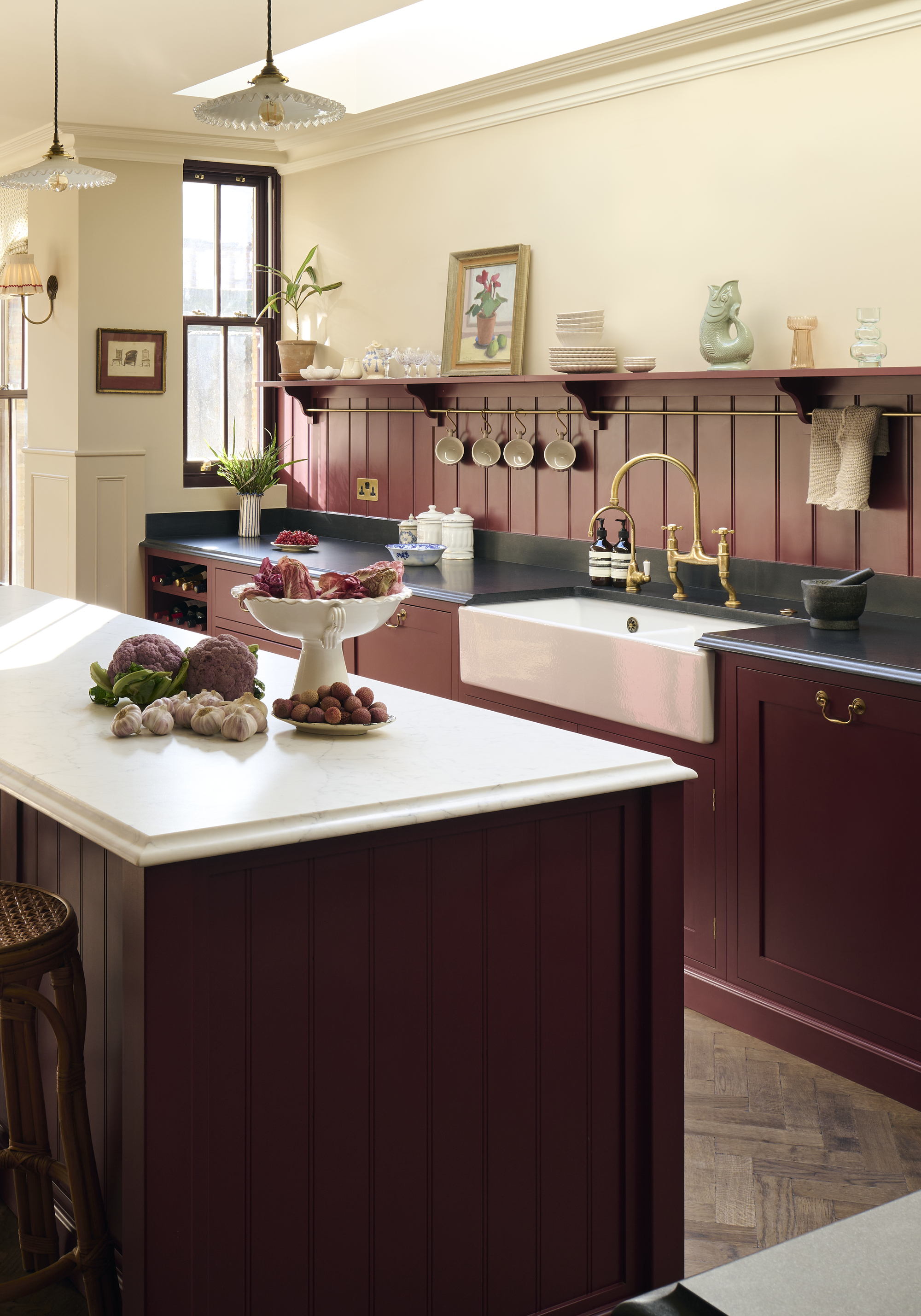A kitchen with burgundy cabinetry, a burdgundy tongue and groove panelled backsplash, and a burgundy kitchen island with a white countertop with ogee edges