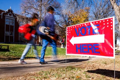 students walking past vote here sign, photo