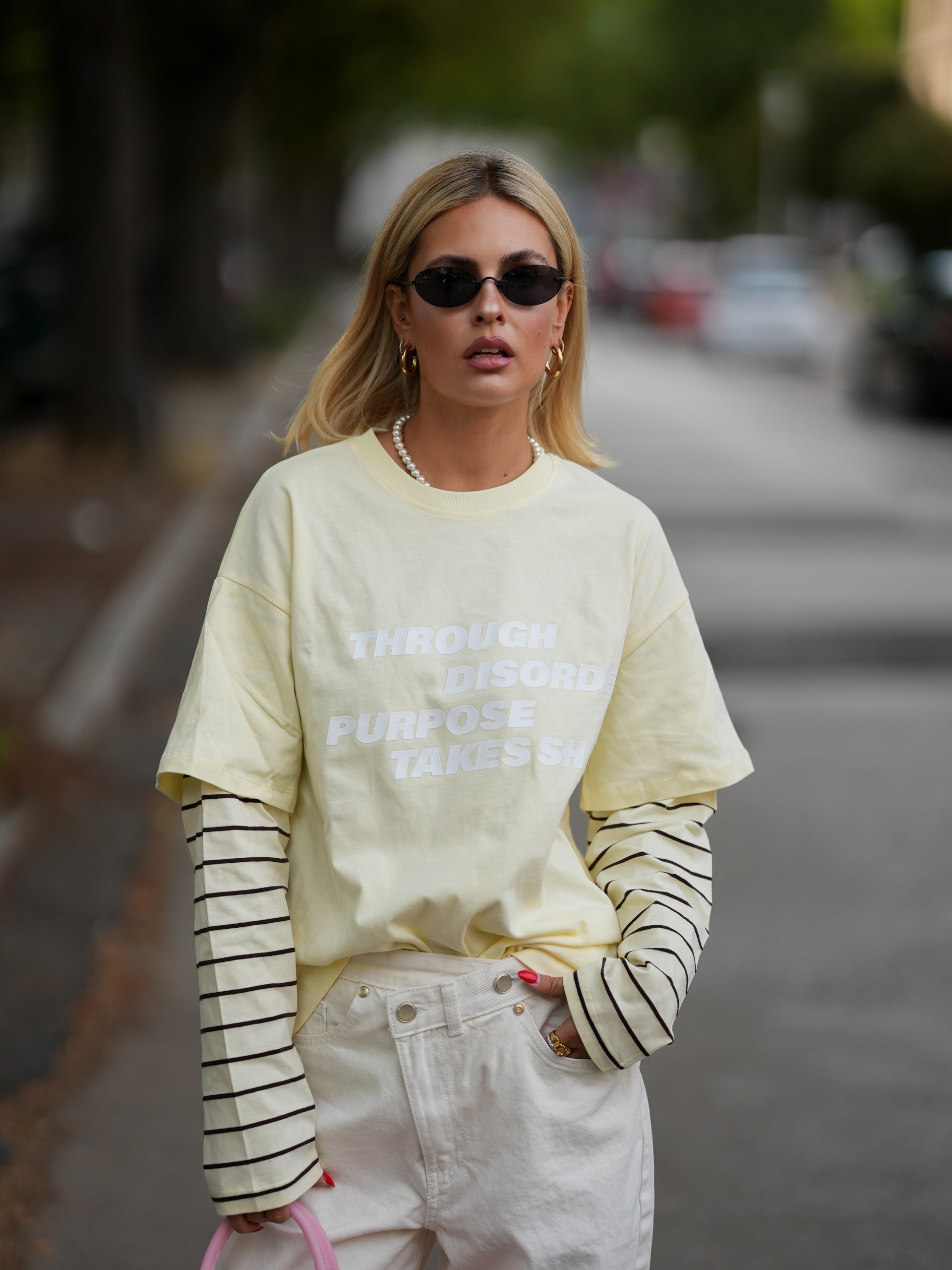 woman street style wearing a layered yellow graphic tshirt with white jeans and black sunglasses.