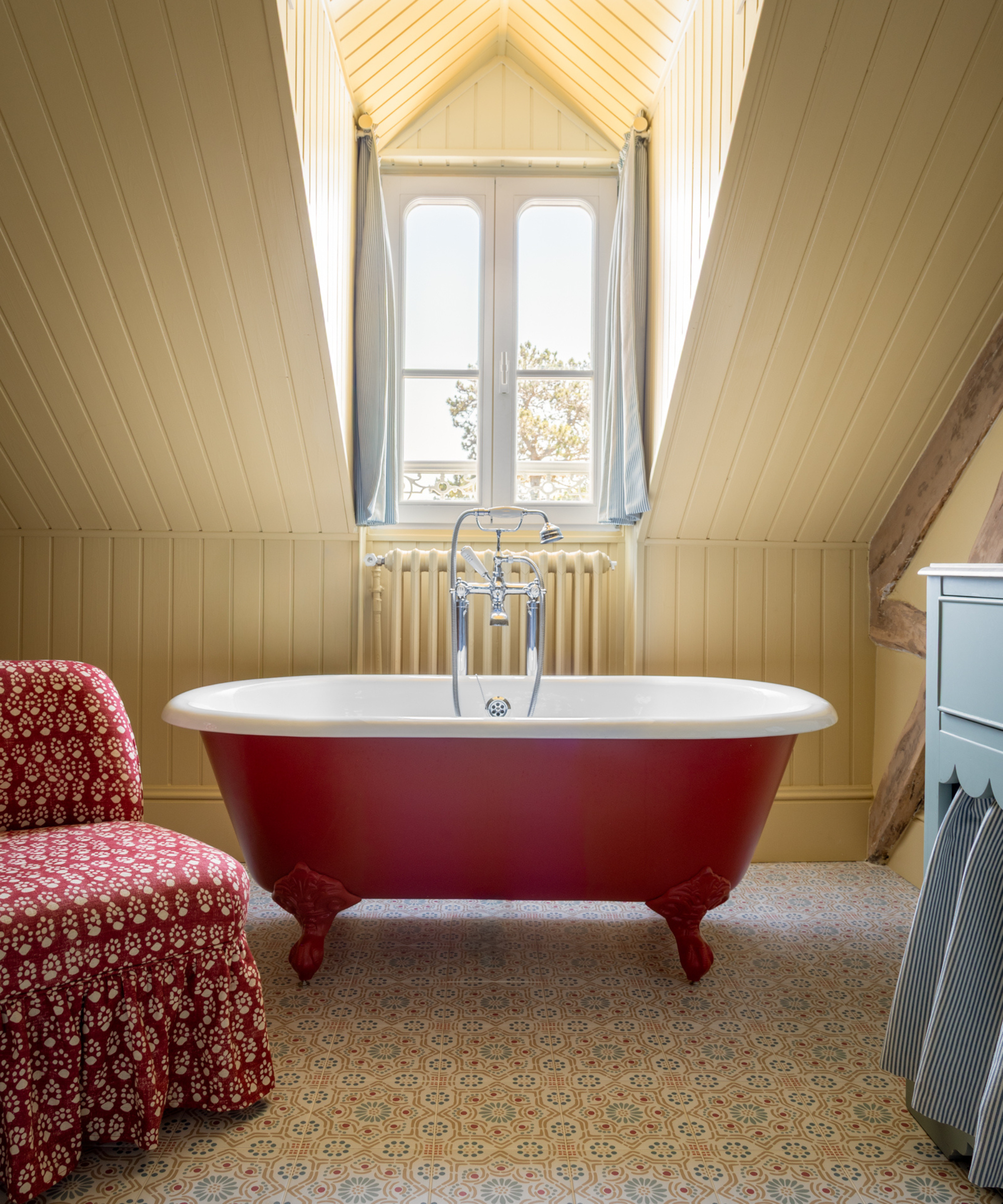 a bathroom with a clawfoot red tub, a patterned red chair, and yellow painted walls