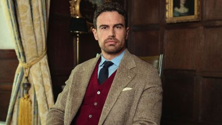 Theo James sits in a wooden chair