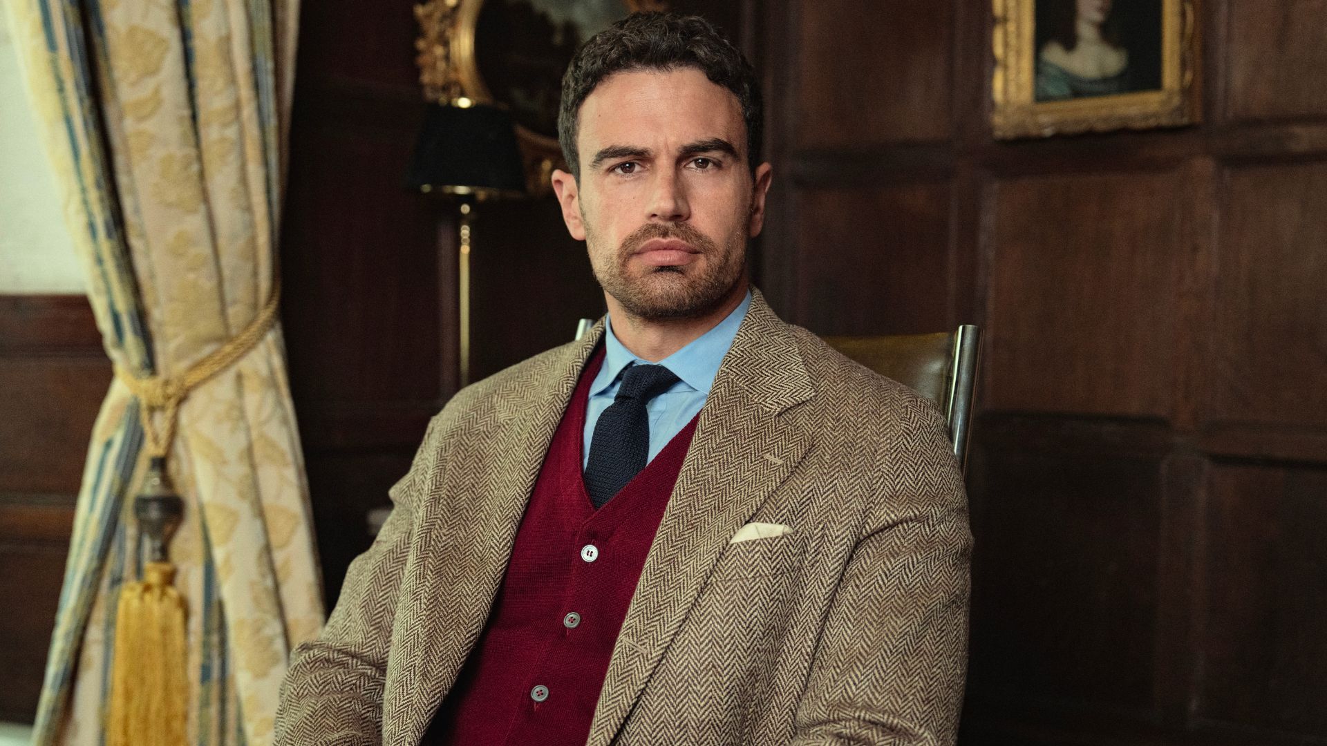 Theo James sits in a wooden chair