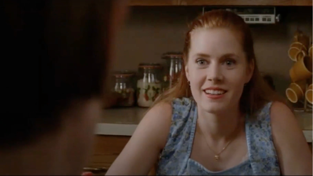 Amy Adams sits with a smile while asking questions in the kitchen in Junebug.