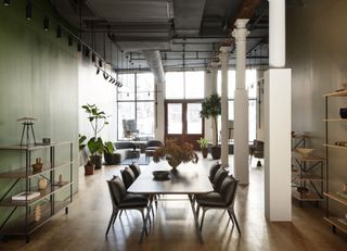 Showroom view with large dining table and chairs, the space's architecture includes white columns and large windows at the back