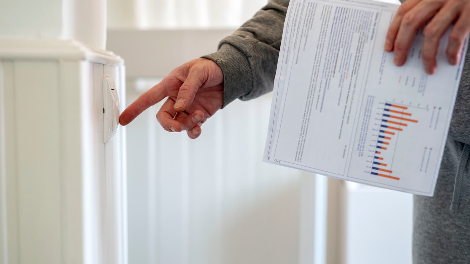 A man turns on a switch with an electricity bill in his hand