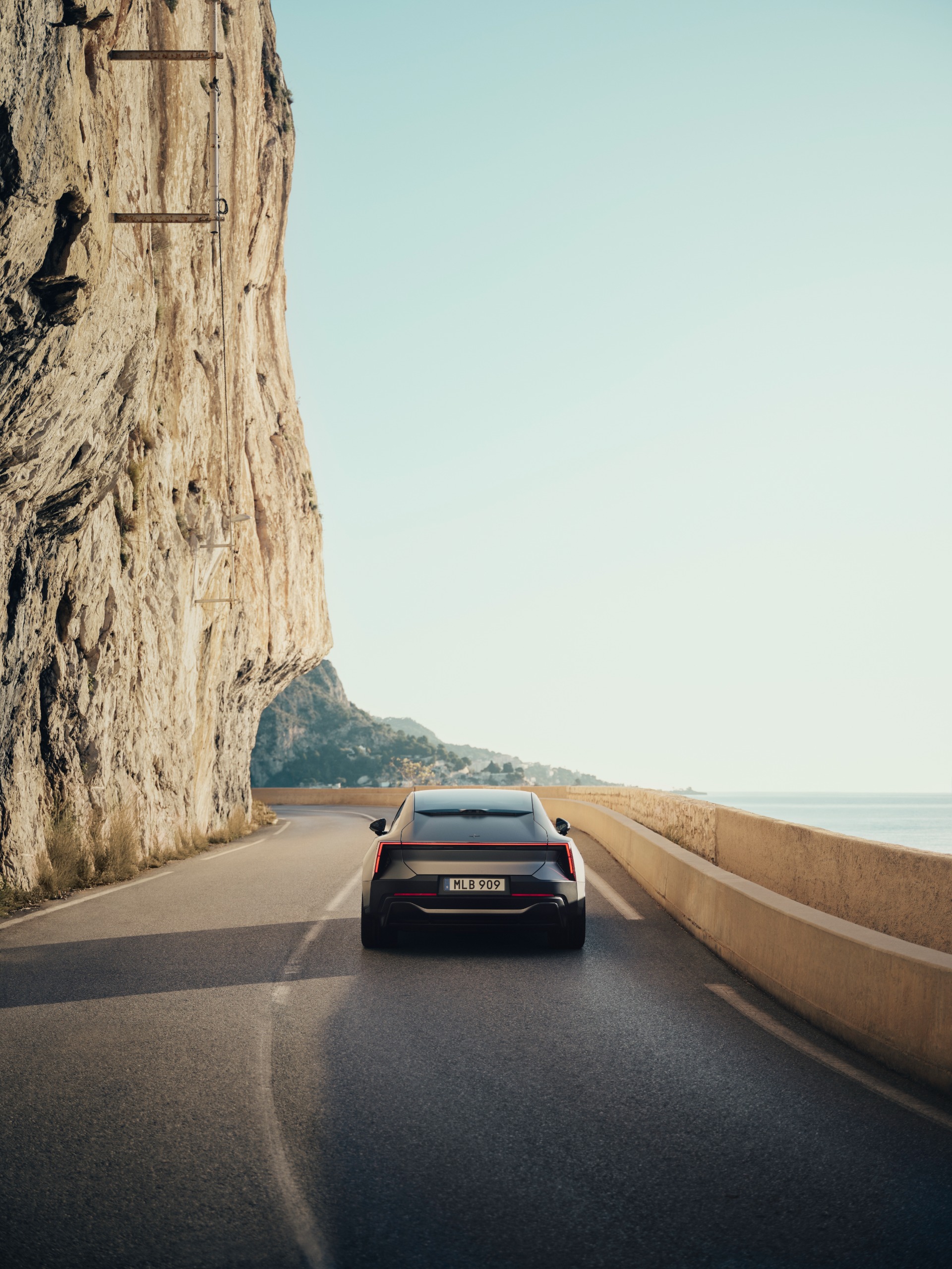 Polestar 5, from the rear, driving along a road with a cliff behind