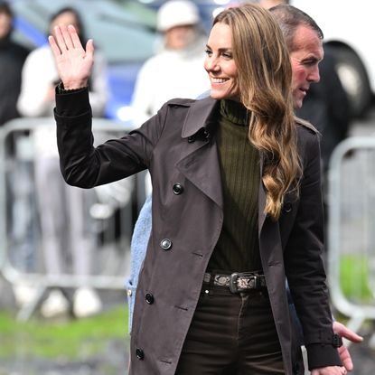 Princess Kate wearing a brown trench and skinny jeans, waving