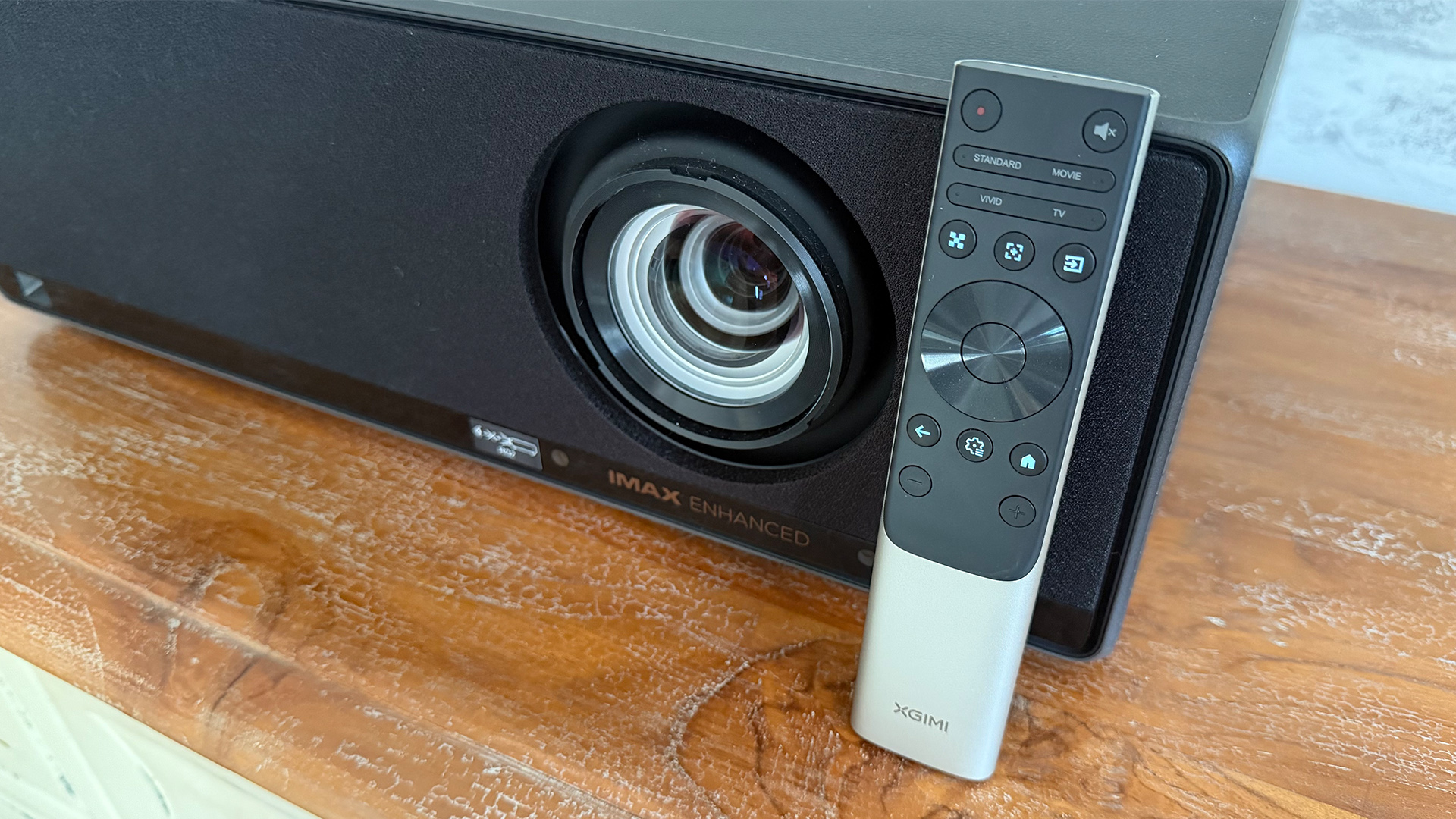 Xgimi Titan home cinema projector on wooden sideboard with remote control leaning against it next to lens